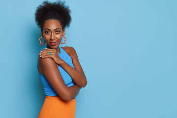 Side view of young black woman standing in head to shoulder pose against blue background with smile, wearing blue top and yellow skirt, good mood concept, copy space