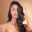 © Ilzer/peopleimages.com - Portrait, indian woman and beauty in studio of curly hair, aesthetic glow and skincare on brown background. Face of model, wavy hairstyle texture and shampoo for keratin, dermatology and cosmetics