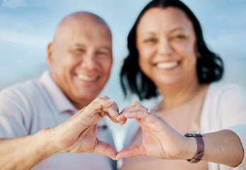 Sticker - Heart shape, hands and mature couple at the beach on a romantic vacation, adventure or holiday. Smile, emoji and portrait of man and woman in retirement with love or support gesture by ocean on trip.