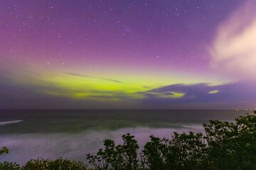 Aurora Australis or southern lights in Dunedin, New Zealand; beautiful purple, pink and green lights, with colourful clouds, fog ocean, night sky and mountains in the background