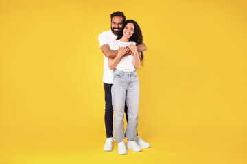 Wall Mural - Beautiful middle eastern couple posing embracing on yellow studio background