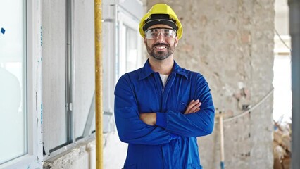 Canvas Print - Young hispanic man worker wearing hardhat standing with arms crossed gesture at construction site