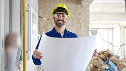 Canvas Print - Young hispanic man worker wearing hardhat reading house project at construction site