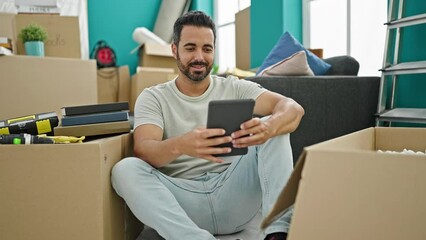 Poster - Young hispanic man using touchpad sitting on floor at new home