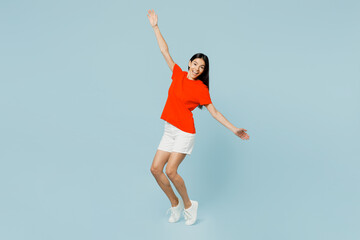 Wall Mural - Full body young latin woman she wear orange red t-shirt casual clothes stand on toes leaning back with outstretched hands dance have fun isolated on plain light blue cyan background Lifestyle concept