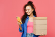 © ViDi Studio - Young woman of African American ethnicity she wear blue shirt casual clothes hold stack cardboard blank boxes use mobile cell phone isolated on plain pastel pink background studio. Lifestyle concept.