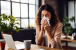 © AspctStyle - Sick young businesswoman using a tissue while sneezes while walking in office