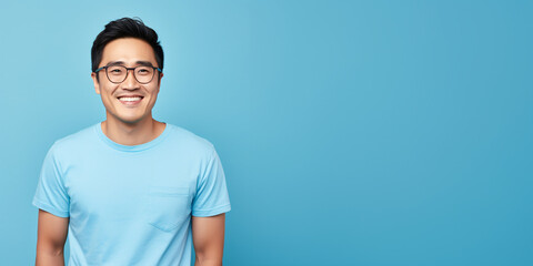 Attractive asian man wearing blue tshirt and glasses. Isolated on blue background.