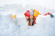 Group of children play in snow fort made of ice blocks. Active winter outdoor games. Castle for snowballs battles. Knitted winter hats.