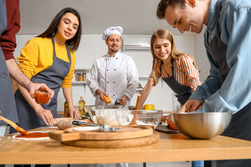 Wall Mural - Group of young people with Italian chef preparing pizza during cooking class in kitchen