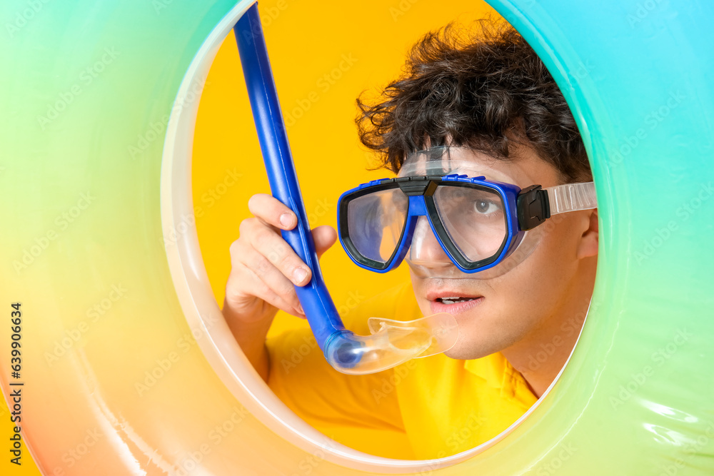 Young man in snorkeling mask with inflatable ring on yellow background, closeup