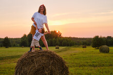 Happiness Is Found In The Simplicity Of Nature As A Woman With Baby Boy Standing On A Hay Bale During Sunset. Portrait Of A Happy Kid Two Years Old And A Woman Thirty Five Years Old