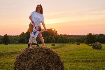 Happiness is found in the simplicity of nature as a woman with baby boy standing on a hay bale during sunset. Portrait of a happy kid two years old and a woman thirty five years old