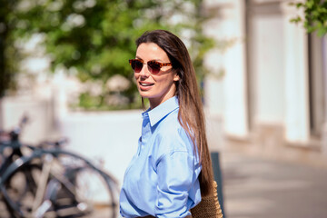 Wall Mural - Attractive brunette haired woman wearing sunglasses and walking on the street