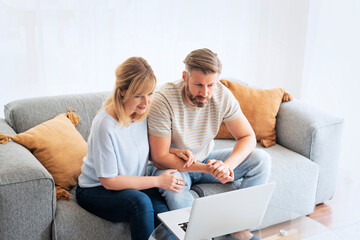 Wall Mural - Middle-aged couple wearing casual clothes and sitting at home on the sofa and using a laptop