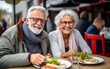 Couple of elderly seniors eat street food in a cafe and have fun
