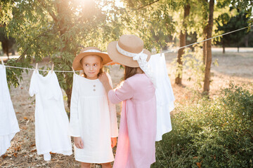 Two child girls playing having fun hanging white bed sheets on rope outdoor. Childhood. Friendship.