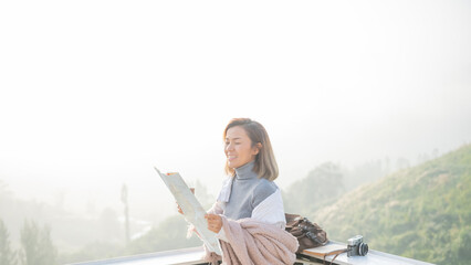 Wall Mural - Girl tourist in mountain read the map and looking mountain view at countryside homestay in the morning sunrise with copy space. journey, trip and relaxing concept. coats blankets in winter.