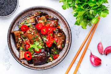 Marinated grilled eggplant with red chili peppers, parsley, sesame seed, soy sauce and garlic, white table background, top view