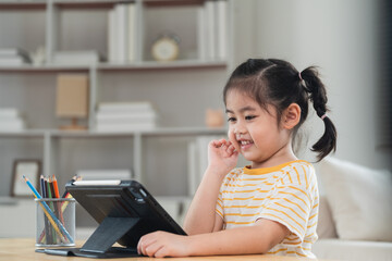 Wall Mural - Asian girl looking and touch on white screen at the tablet screen attentively. overstimulated children concept. Too much screen time. Cute girl watching videos while tv, Internet addiction concept.