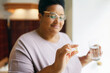 © shurkin_son - Selective focus on hand of black senior plus size woman holding transparent capsule of polyunsaturated fatty acid and glass of water, taking food supplements for healthy heart and nerve system