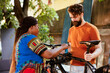 Youthful and athletic interracial couple fixing damaged bicycle outside for summer leisure cycling. Healthy black woman helping caucasian man by clamping bike frame to repair-stand for easy repairing.