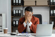 © NINENII - Young sad businessman is sitting at table, covering his face with his hand. On desk is laptop, tablet computer, Stress.