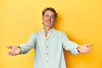 Wall Mural - Middle-aged man posing on a yellow backdrop showing a welcome expression.
