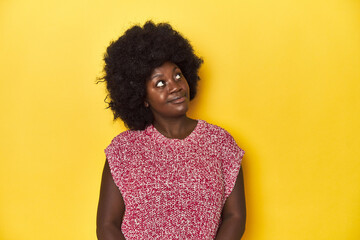 Wall Mural - African-American woman with afro, studio yellow background relaxed and happy laughing, neck stretched showing teeth.