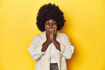 Wall Mural - African-American woman with afro, studio yellow background laughing about something, covering mouth with hands.