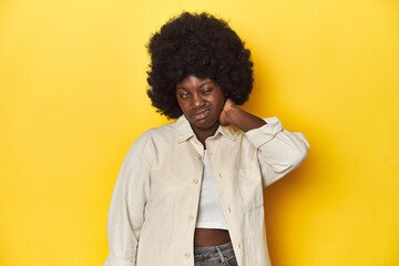 Wall Mural - African-American woman with afro, studio yellow background having a neck pain due to stress, massaging and touching it with hand.