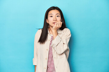 Wall Mural - Asian woman in layered shirt and striped t-shirt, biting fingernails, nervous and very anxious.