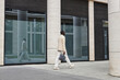 © Seventyfour - Long shot of young African American businessman in white suit carrying handbag while walking along modern architecture with large windows