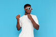 © Богдан Маліцький - african american man in white t-shirt and sunglasses dances to music and sings on blue isolated background