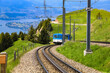 Nice view of the blue cogwheel railway train ascending the Rigi Kulm mountain station. In the background you can see the beautiful mountainous landscape with Lake Lucerne (Vierwaldstättersee).