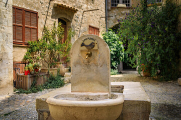 Poster - Traditional old stone fountain on a square in the medieval town of Saint Paul de Vence, French Riviera, South of France with a sign for drinking water