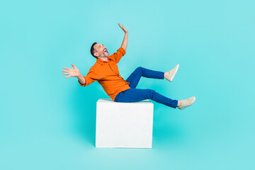 Wall Mural - Portrait of careless playful man dressed orange shirt falling from platform look empty space isolated on turquoise color background