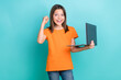 © deagreez - Photo of overjoyed little girl wear orange stylish t-shirt raising fist holding laptop pass exam isolated on teal color background