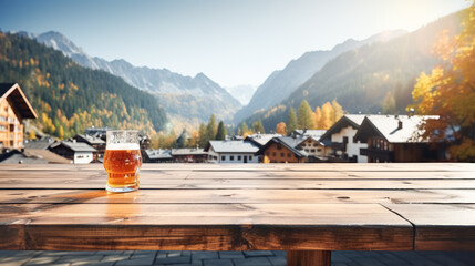 Wall Mural - Wooden table top showcase with mug of beer on alpine village background, holiday flags, blank bokeh background