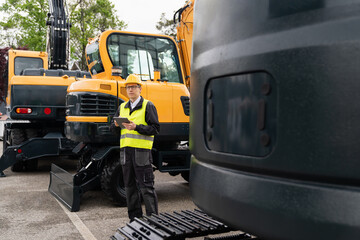 Aufkleber - Engineer in a helmet with a digital tablet stands next to construction excavators.