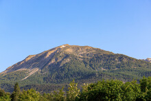 A Scenic View Of A Majestic Mountain Summit With Some Snow Spot Left (Mont Guillaume) With Pine Trees Forest Under A Majestic Blue Sky