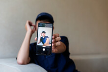 Teenage Boy Holding A Smart Phone In Front Of His Face At Home, Taking Selfies With His Smartphone, Digital Display On Foreground, Teen With His Own Portrait In Smartphone, Teen Blogging