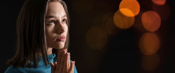 Praying young woman on dark background with space for text
