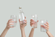 Female Hands With Bottle And Glasses Of Cold Water On Light Background