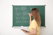 © Pixel-Shot - Young math teacher with book writing on blackboard in classroom