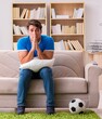© Elnur - Man watching football at home sitting in couch