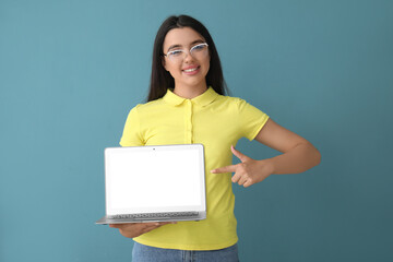 Poster - Happy young female programmer pointing at laptop on blue background