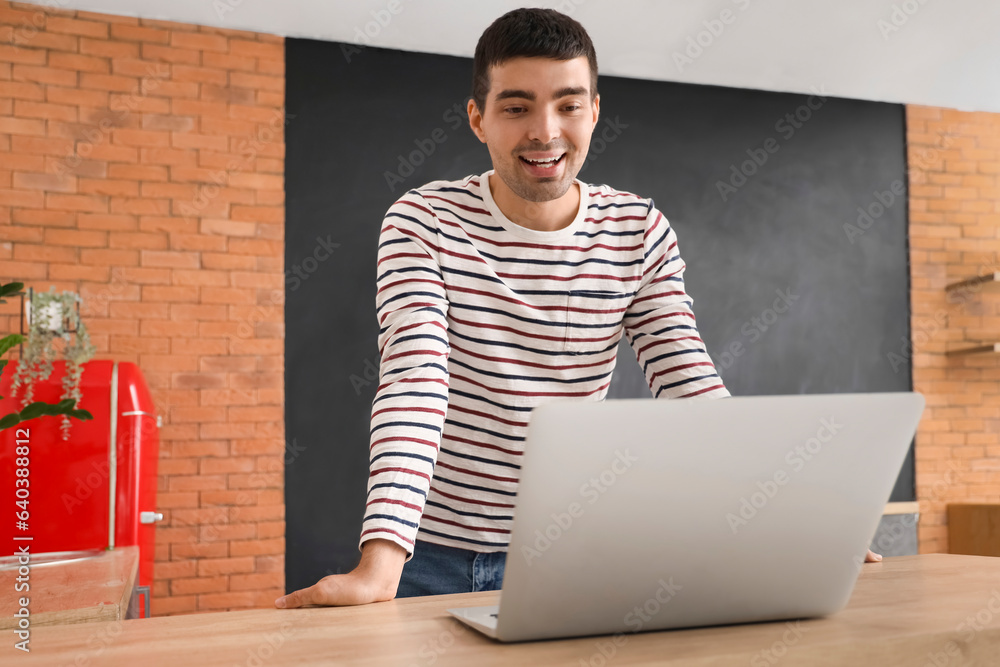 Young man with laptop video chatting in kitchen