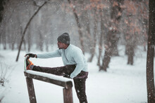 Young Fit And Athletic African Man Stretching Before Running And Exercising On A Forest Trail During Winter And Snow