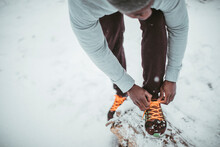 Young Athletic And Fit African Man Tying His Shoelaces And Getting Ready To Go Jogging And Exercising On A Forest Trail During Winter And Snow
